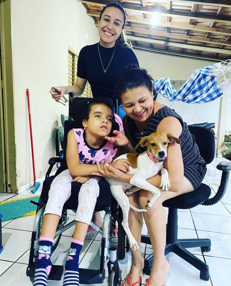 Eva e Luziane sentadas com Luna no colo e a protetora Bruna, que ajudou na adoção — Foto: Divulgação