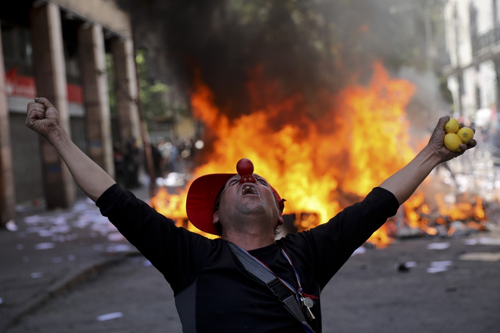 Manifestante vestido de palhaço grita em frente a barricada no centro de Santiago, no Chile, nesta terça-feira (22) — Foto: Rodrigo Abd/AP Photo