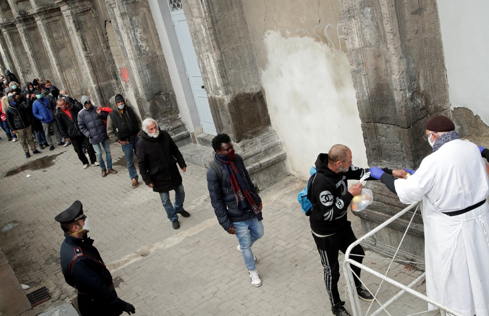Em Napoles, na Itália, padre entrega comida aos sem teto, que fazem fila com espaços para evitar contágio, em 27 de março de 2020 — Foto: Ciro De Luca/Reuters