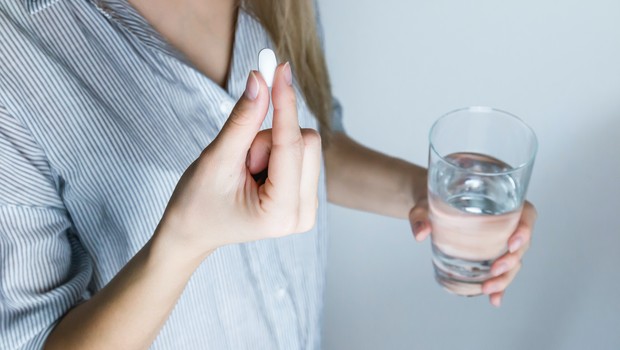 mulher segurando comprimido e copo de água (Foto: pexels)