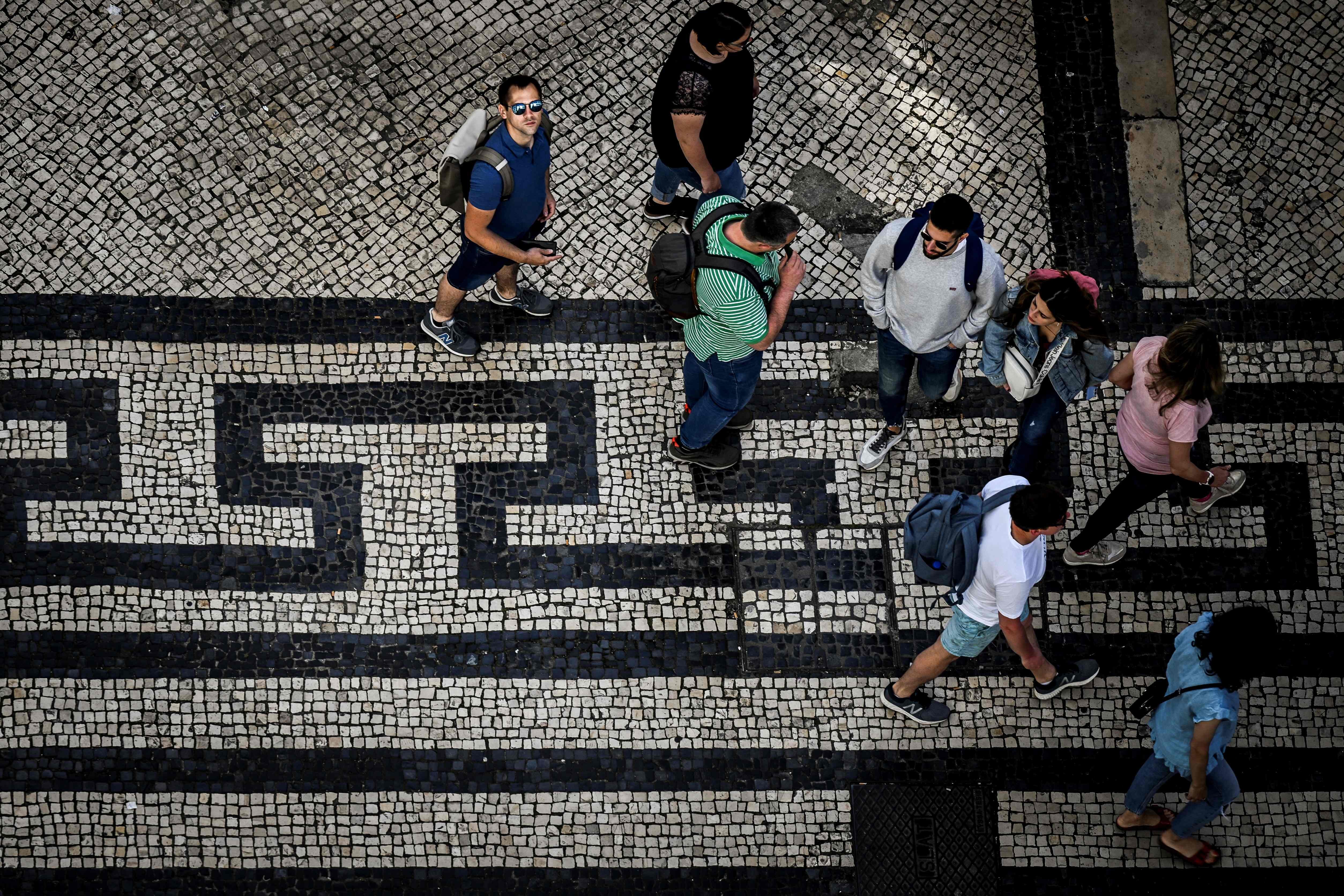 Pedestres caminham em uma calçada de pedras portuguesas em Lisboa