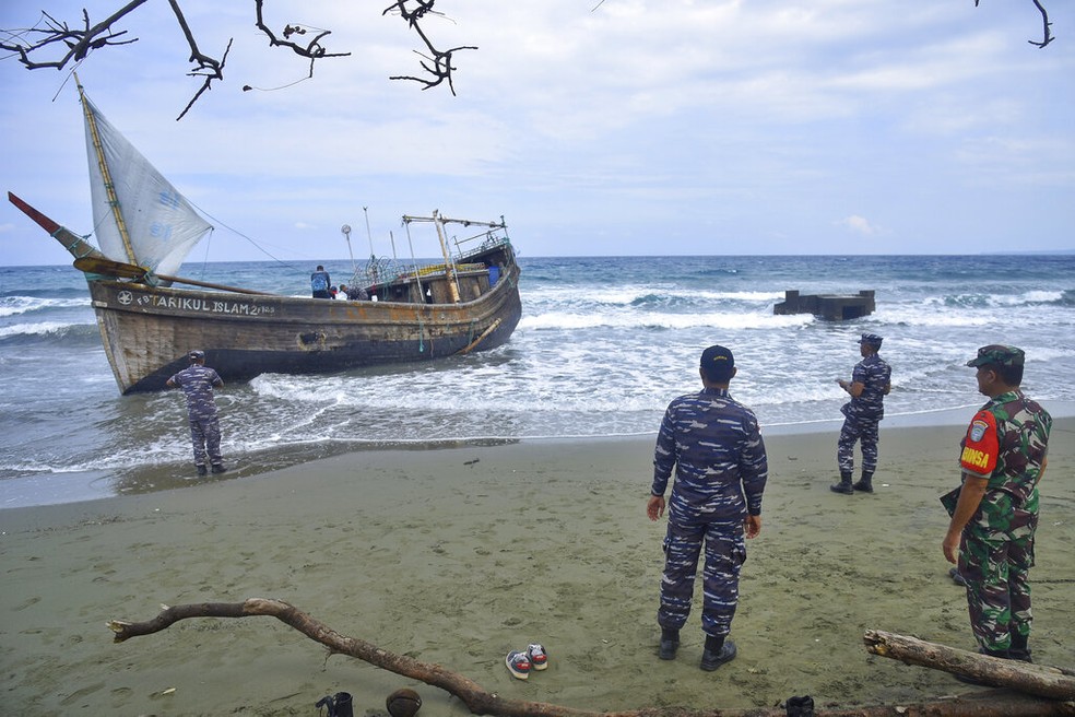 Homens da guarda costeira da Indonésia observam barco de madeira no qual um grupo de rohingyas chegou à praia de Indra Patra, no norte da Indonésia, em 25 de dezembro de 2022. — Foto: Rahmat Mirza/ AP