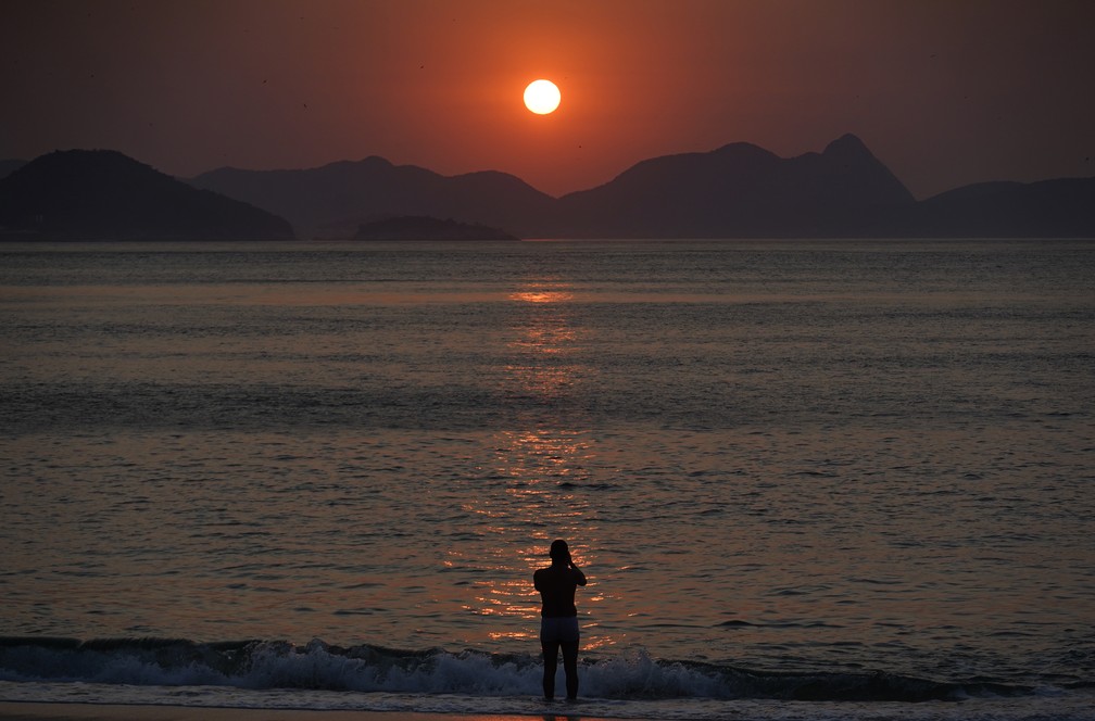 Homem entra na água para registrar o nascer do sol no dia que pode ser o mais quente do ano no Rio — Foto: Marcos Serra Lima/G1