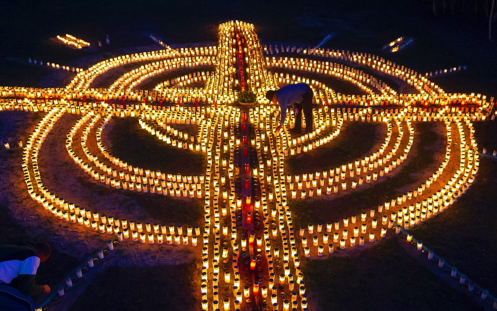 Mulher acende velas que formam cruz gigante em memória aos mortos por Covid-19 em Zella-Mehlis, na Alemanha, em 17 de abril de 2020 — Foto: Jens Meyer/AP