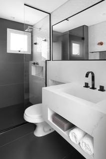 No banheiro projetado pelo Studio Deux Arquitetura, o boxe até o teto apresenta um recorte para acompanhar a estrutura, valorizada pelo contorno preto