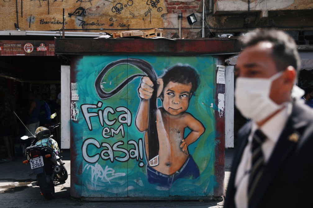 Homem de máscara passa por grafite em um muro no Rio de Janeiro que diz 'fica em casa!' no dia 2 de setembro. — Foto: Pilar Olivares/Reuters