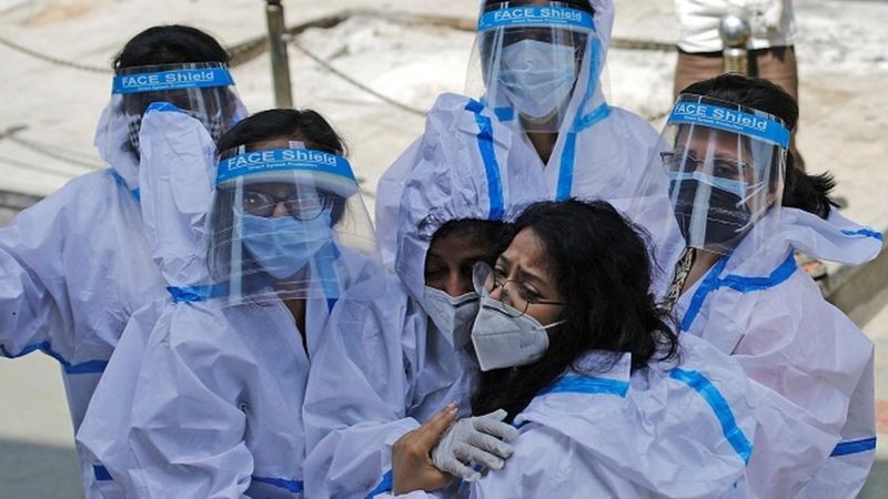 Grupo de trabalhadoras da saúde com equipamento de proteção individual se abraça (Foto: Reuters via BBC)