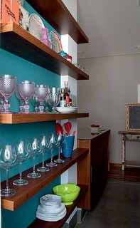 O apartamento de 60 m² tinha uma cozinha bem estreita. Em uma parede vazia, a arquiteta Gabriela Marques projetou prateleiras finas, onde a moradora expõe taças e vasos