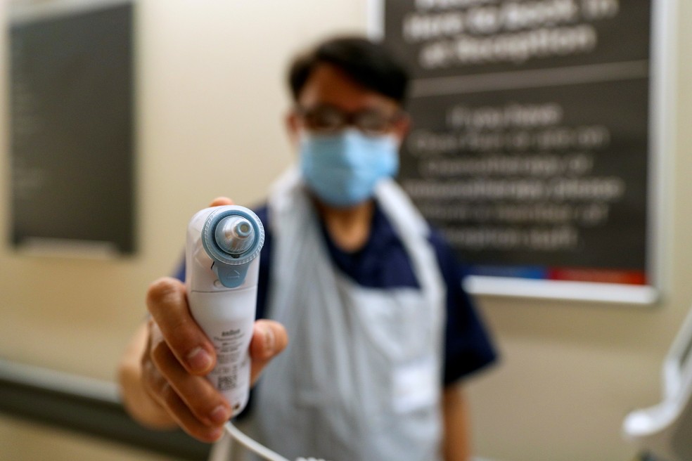 Enfermeiro com equipamento de proteção segura termômetro para medir a temperatura das pessoas que chegam a um hospital em Slough, a oeste de Londres, na Inglaterra. — Foto: Steve Parsons / Pool / AFP