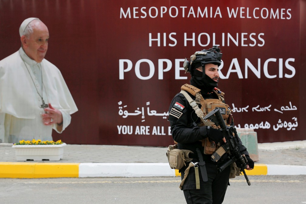 Membro das forças de segurança iraquianas passa diante de cartas de boas-vindas ao Papa Francisco no Iraque — Foto: Reuters/Teba Sadiq