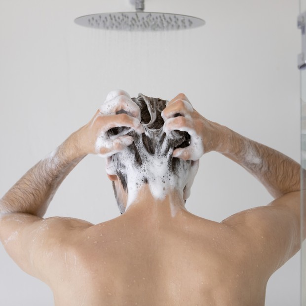 Rear view young man cleaning hair with foamy anti dandruff shampoo close up, standing in modern bathroom at home, taking morning shower, washing head and body, personal hygiene and skincare concept (Foto: Getty Images/iStockphoto)