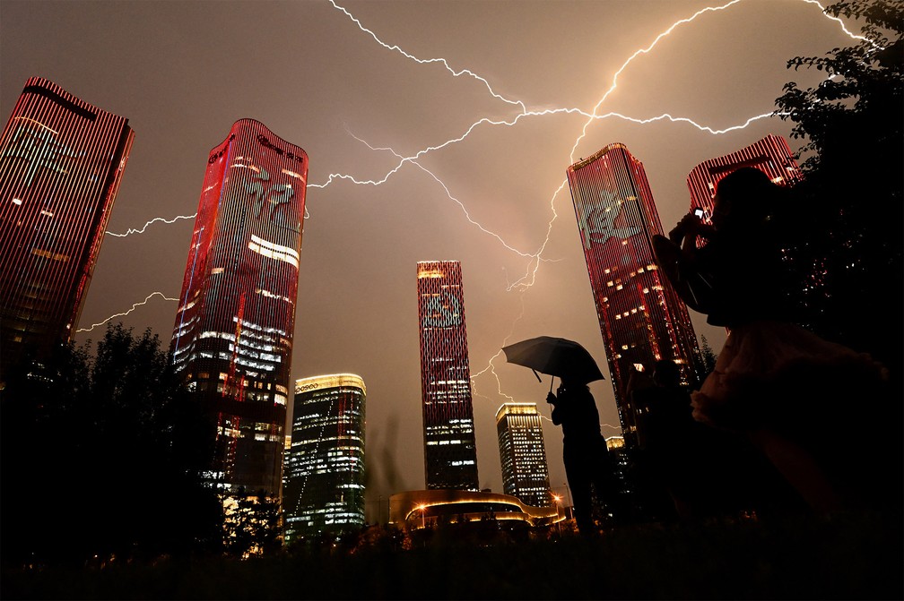 30 de junho - Raios cortam o céu de Pequim enquanto pessoas observam prédios iluminados com homenagem na véspera dos 100 anos do Partido Comunista da China — Foto: Noel Celis/AFP