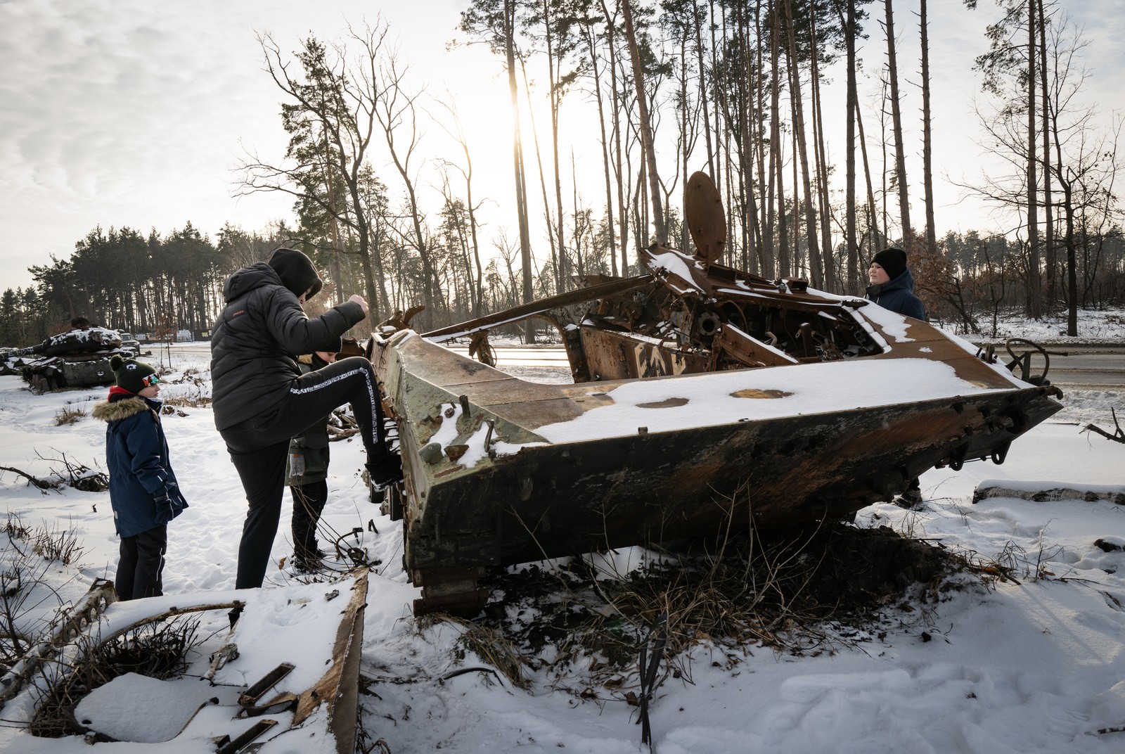 Jovens de Irpin, próximo a Soledar, chutam veículo militar russo destruído, agora coberto de neve, na Ucrânia — Foto: Lynsey Addario/The New York Times