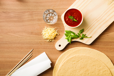 Você vai precisar: copo de vidro, molho de tomate, queijo ralado, manjericão, palitos de churrasco, papel-manteiga e massa para pizza.