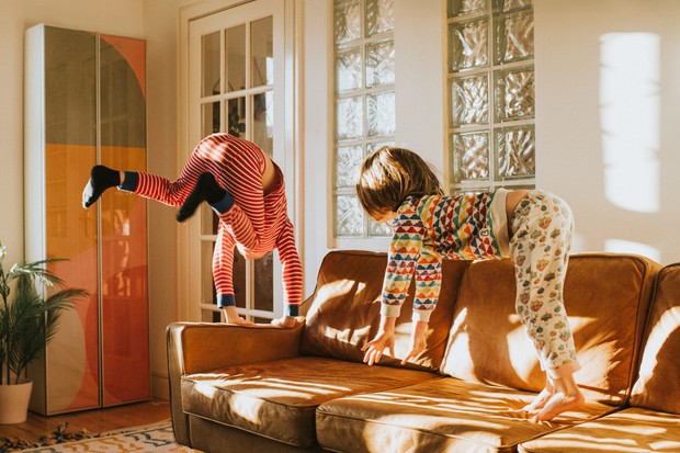 Two cute kids wearing pyjamas bounce on a brown leather couch in a sunny domestic room. Conceptual with space for copy. (Foto: Getty Images)