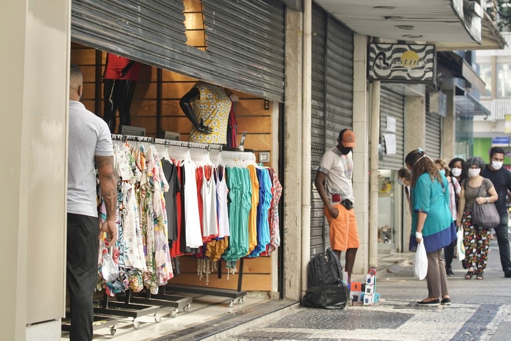 Em Copacabana, loja de roupas com metade da porta aberta; camelô oferece produto na calçada  — Foto: Marcos Serra Lima/ G1