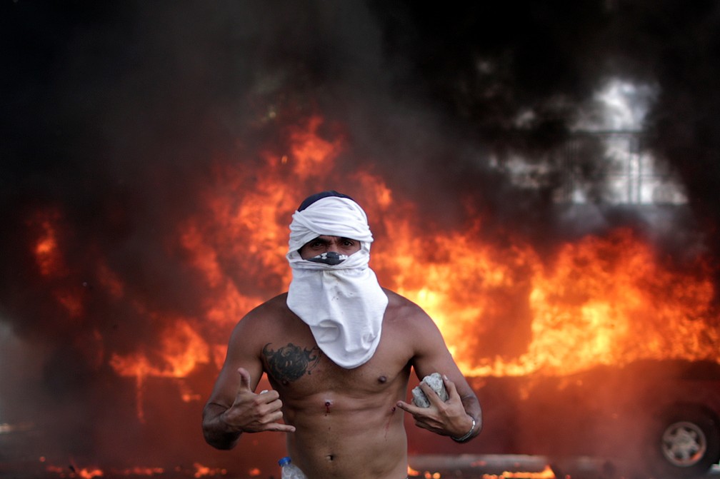 Manifestante ferido caminha diante de Ã´nibus incendiado em Caracas, na Venezuela, no dia 30 de abril â€” Foto: Ueslei Marcelino/Reuters