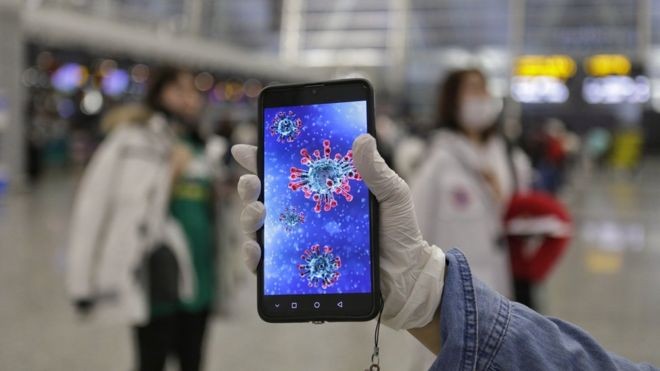 Passageiro mostra ilustração do coronavírus em seu celular no aeroporto de Guangzhou, na província chinesa de Guangdong (Foto: EPA via BBC News)