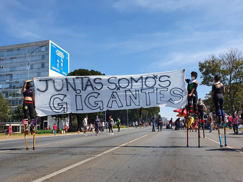 Mulheres sobre pernas de pau participam de protesto contra Bolsonaro, em Brasília, com faixa dizendo "Juntas somos gigantes" — Foto: Anna Reis/ TV Globo