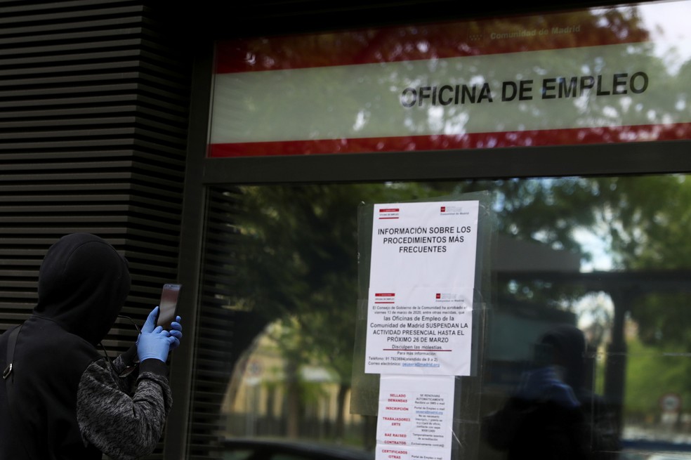 Homem tira foto de painel de informações do lado de fora de um centro de emprego governamental fechado para o público por causa da pandemia provocada pelo coronavírus, em Madri, na Espanha, na terça-feira (28)  — Foto: Susana Vera/Reuters 