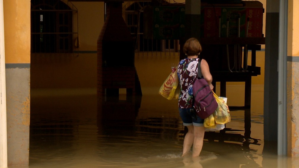 Mulher salva alguns pertences e olha para casa tomada pela água em Cariacica, ES — Foto: Reprodução/TV Gazeta