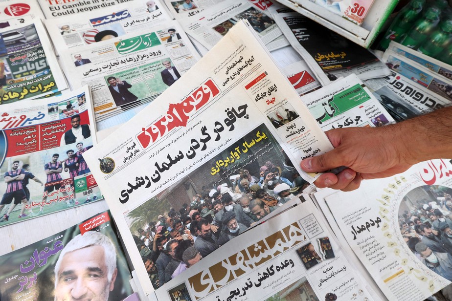 Um homem mostra a edição de hoje dos jornais iranianos com o título da primeira página em farsi: 'Faca no pescoço de Salman Rushdie'