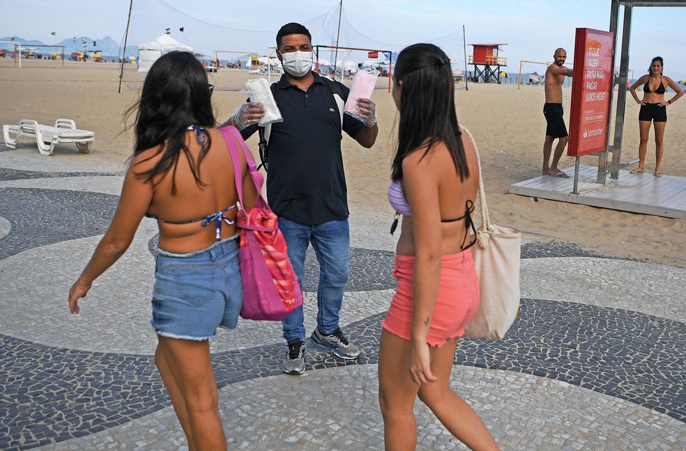 Vendedor oferece máscaras enquanto duas mulheres caminham em calçada na praia de Copacabana, no Rio de Janeiro, em 16 de março de 2020. — Foto: Carl de Souza / AFP