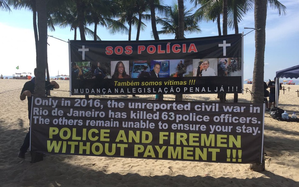 Cartazes do protesto realizado na Praia de Copacabana contra a morte de policiais traz frazes em inglês que evidenciam o sacateamento da corporação no estado. Em 2016, foram 63 mortes, segundo a entidade (Foto: Matheus Rodrigues/G1)