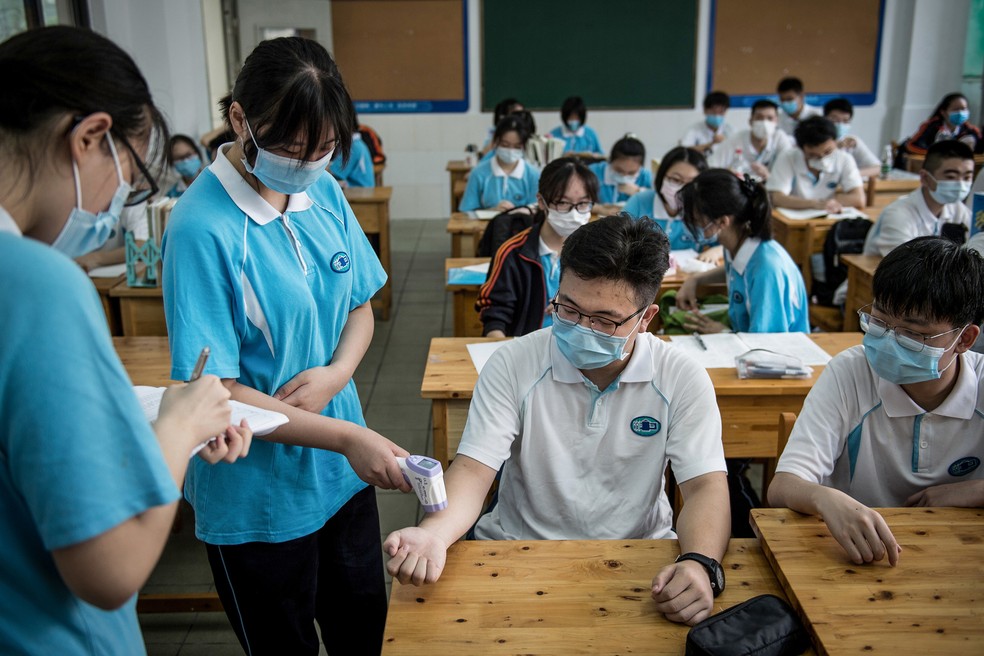 10 de julho - Aluna verifica temperatura corporal de seus colegas de classe em sala de aula de escola secundária, em Wuhan, na província central de Hubei, na China. As escolas secundárias em Wuhan reabriram em 10 de julho, após o início do prazo ter sido adiado devido ao surto de doença por coronavírus (Covid-19) — Foto: STR/AFP