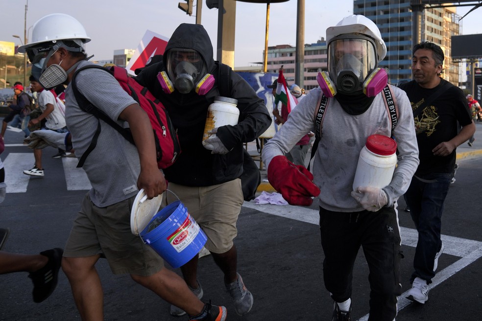 Os chamados ‘desativadores’ carregam grandes garrafas plásticas cheias de uma mistura de água, bicarbonato de sódio e vinagre, para neutralizar o efeito das bombas de gás lacrimogênio durante confrontos com a polícia em Lima, Peru — Foto: Martin Mejia/AP