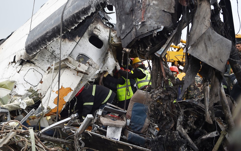 Funcionários trabalham entre os destroços do avião da US-Bangla Airlines que caiu no aeroporto de Katmandu, no Nepal, na segunda-feira (12) (Foto: Prakash Mathema/AFP)