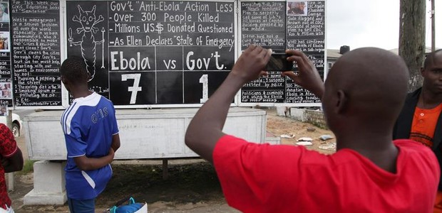 Pessoas passam para olhar notícias sobre o Ebola na capital da Libéria (Foto: Agência EFE)