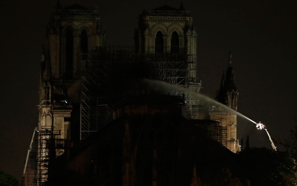Bombeiros jogam água na fachada da Catedral de Notre-Dame, em Paris, na madrugada de terça-feira (16), após controlarem incêndio no local — Foto: Zakaria Abdelkafi/AFP