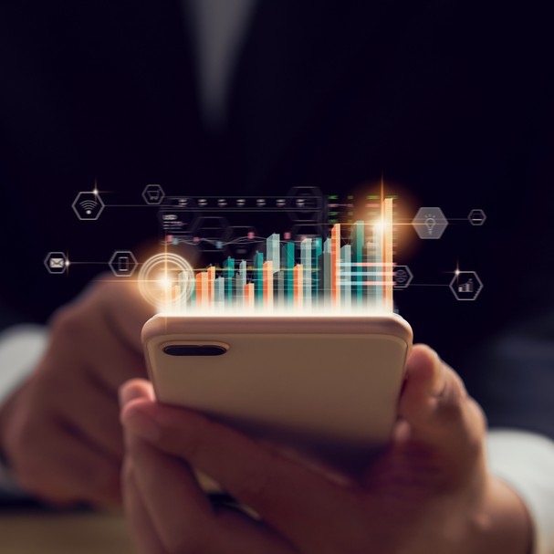 Stock exchange market concept, hand trader holding smartphone with graphs analysis candle line on bokeh colors light in night. (Foto: Getty Images/iStockphoto)