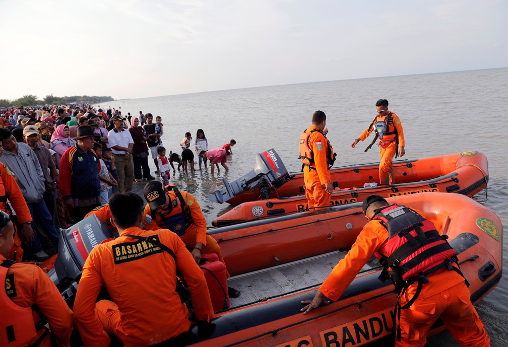 Pessoas na praia assistem a equipe preparar botes para resgate de avião da Lion Air que caiu na Indonésia — Foto: Beawiharta/Reuters