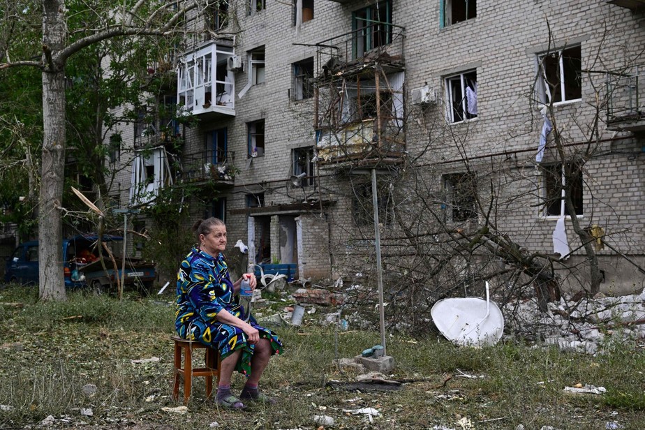 Mulher sentada em frente a seu prédio, parcialmente destruído após ser atingido por um míssil, em Chasiv Yar, Ucrânia