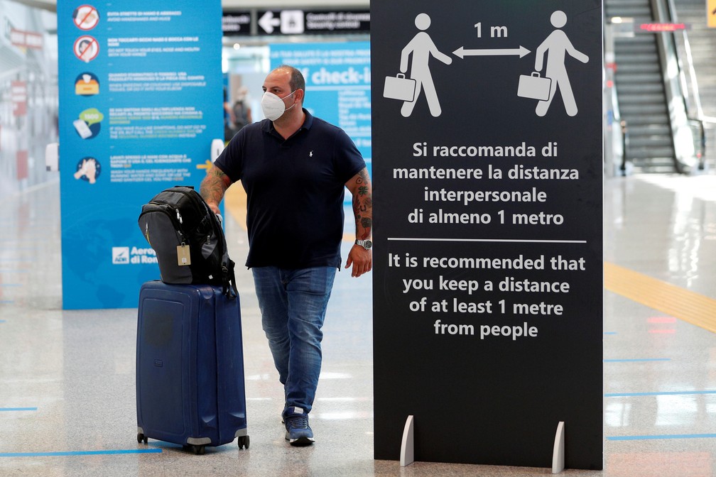 30 de junho - Passageiro com máscara caminha ao lado de placa que pede distanciamento social no aeroporto de Fiumicino, perto de Roma, na Itália — Foto: Guglielmo Mangiapane/Reuters
