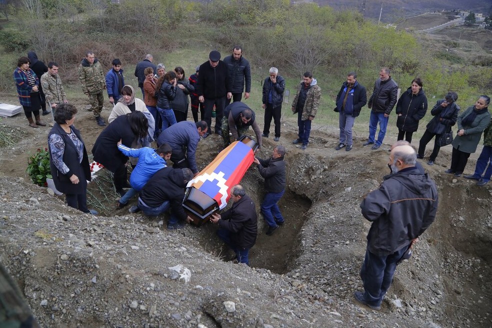 Foto de arquivo mostra familiares enterrando corpo do militar armênio Mkhitar Beglarian, morto nos conflitos em Nagorno-Karabakh. Sobre o caixão, a bandeira do território separatista — Foto: Sergei Grits/AP Photo
