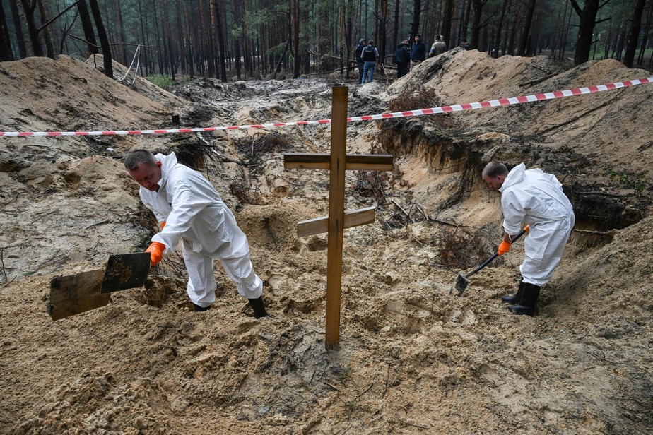 Dois técnicos forenses cavam perto de uma cruz em uma floresta nos arredores de Izium, na Ucrânia, onde foram encontrados mais de 440 corpos em valas comunsa