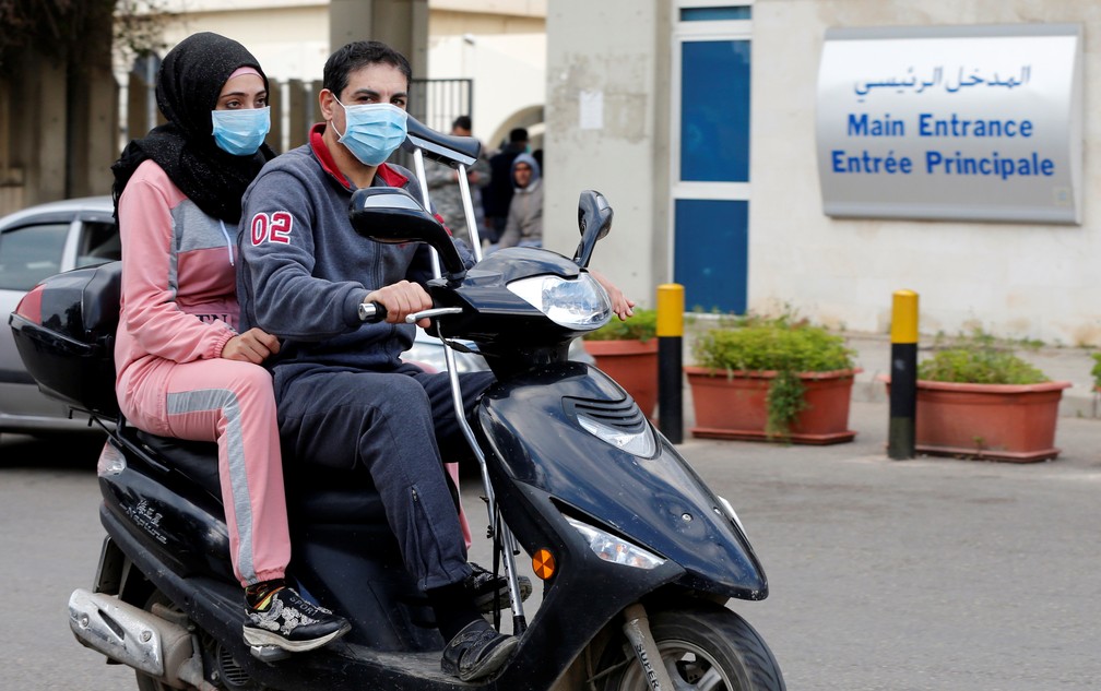 Pessoas usando máscaras protetoras contra o coronavírus passam de moto em frente ao Hospital Rafiq Hariri, em Beirute, no Líbano, onde o primeiro caso detectado no país está sendo mantido em quarentena nesta sexta (21). — Foto: Mohamed Azakir/Reuters