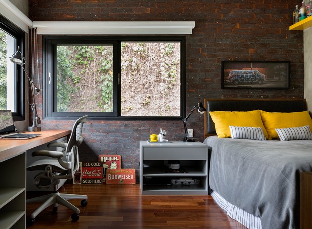 QUARTO | Inspirado em um loft nova-iorquino, o ambiente tem tijolo inglês e cimento queimado nas paredes, além dos detalhes em amarelo. Bancada, criado-mudo e prateleira laqueados, da REM Marcenaria. Cadeira Aeron, da Hermann Miller. Quadros da Urban Arts (Foto: Julia Ribeiro/Divulgação)