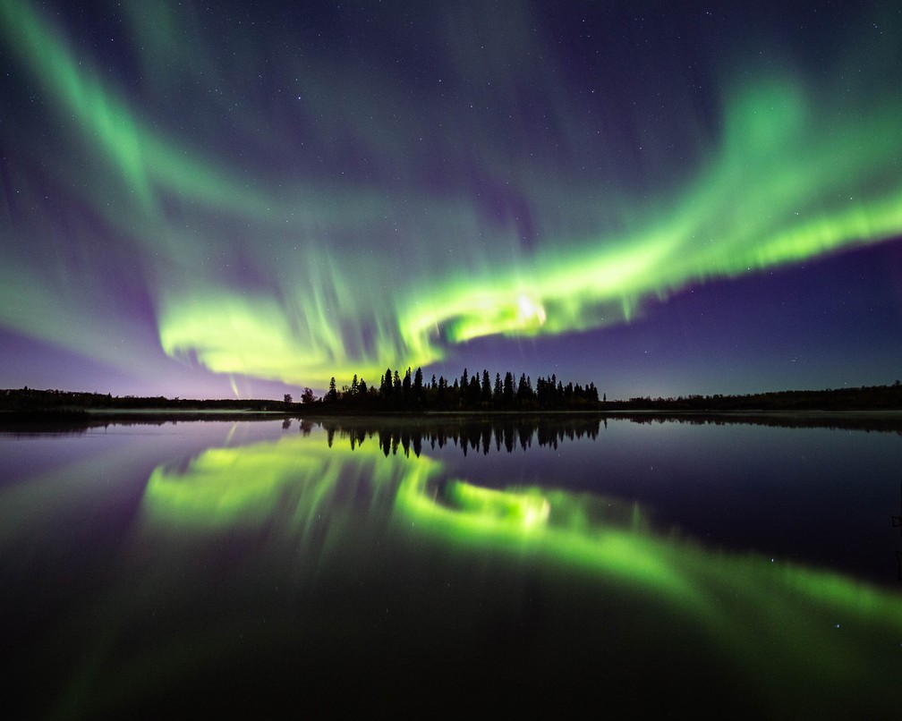 Aurora boreal é refletida em um lago em Alberta, no Canadá. — Foto: Carl Gallagher