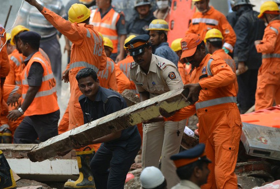 Policial e integrante das equipes de resgate removem entulho na busca de sobreviventes após desabamento de prédio em Mumbai, na Índia, nesta quinta-feira (31)  (Foto: Punit Paranjpe / AFP)