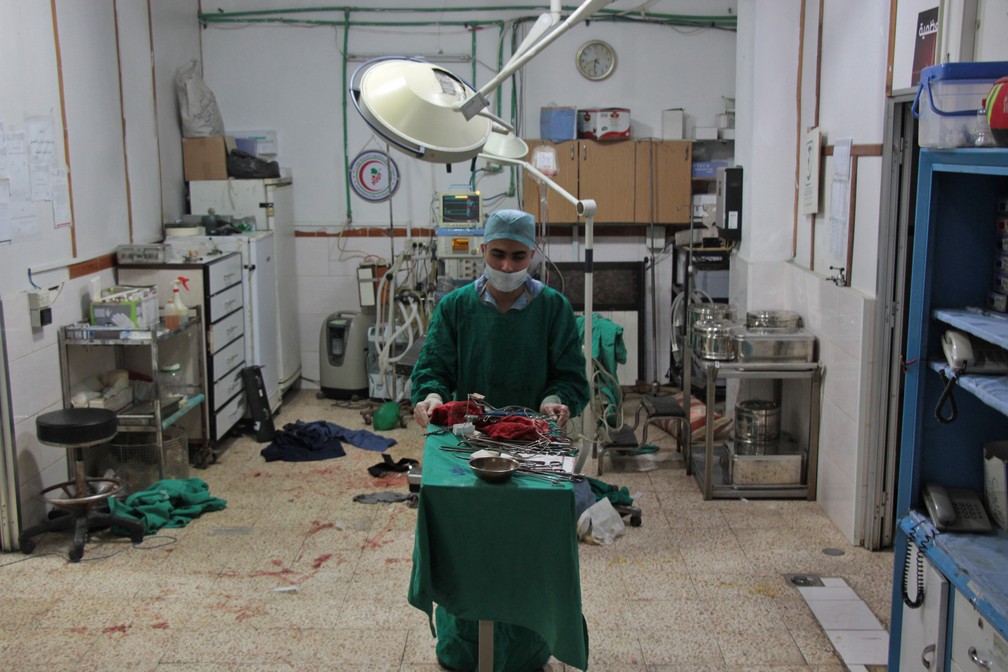 Cirurgião carrega material usado após operação em hospital em Duma, na Síria. Equipamento, que deveria ser descartável, é reutilizado (Foto: Hamza Al-Ajweh/AFP)