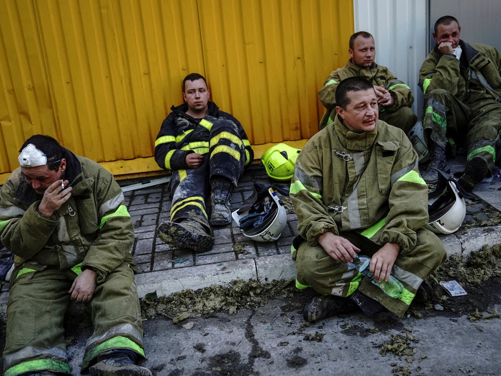 Socorristas ucranianos sentados na calçada após passar horas buscando sobreviventes em Kremenchuk — Foto: Anna Voitenko/REUTERS