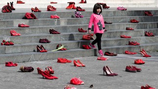 Jovem observa instalação de sapatos vermelhos femininos exibidos em uma escada, como um símbolo para denunciar a violência contra as mulheres, em Tirana, AlbâniaREUTERS