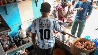Dono de uma barraca de chá usa uma camisa da seleção da Argentina enquanto atende seus clientes em Ichhapur, a cerca de 35 km ao norte de Calcutá — Foto: DIBYANGSHU SARKAR / AFP