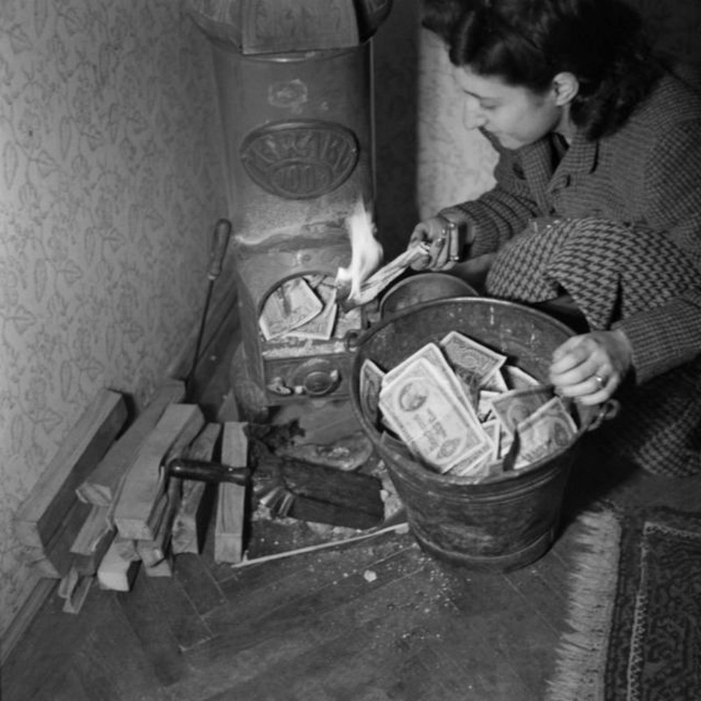 Mulher usando pengős como combustível para a lareira — Foto: Getty Images