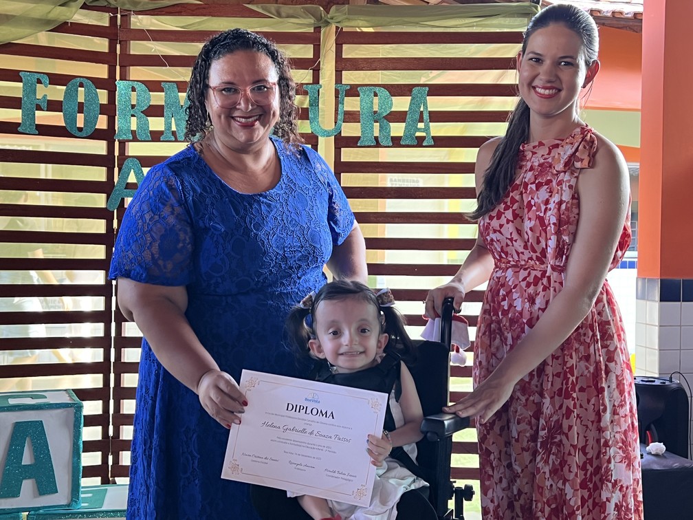 Helena recebendo o diploma das mãos de sua professora e sua cuidadora — Foto: Caíque Rodrigues/g1 RR