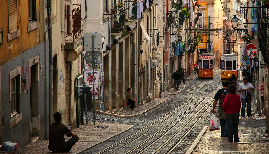Pedestres e bondinhos circulam em uma rua de Lisboa